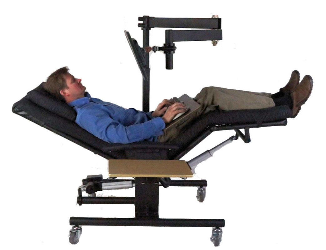 A reclining man lies on a black adjustable medical-style examination table with a mounted tablet screen above him, on a plain white background. Zero Gravity Chair 1a Special Needs Computers.