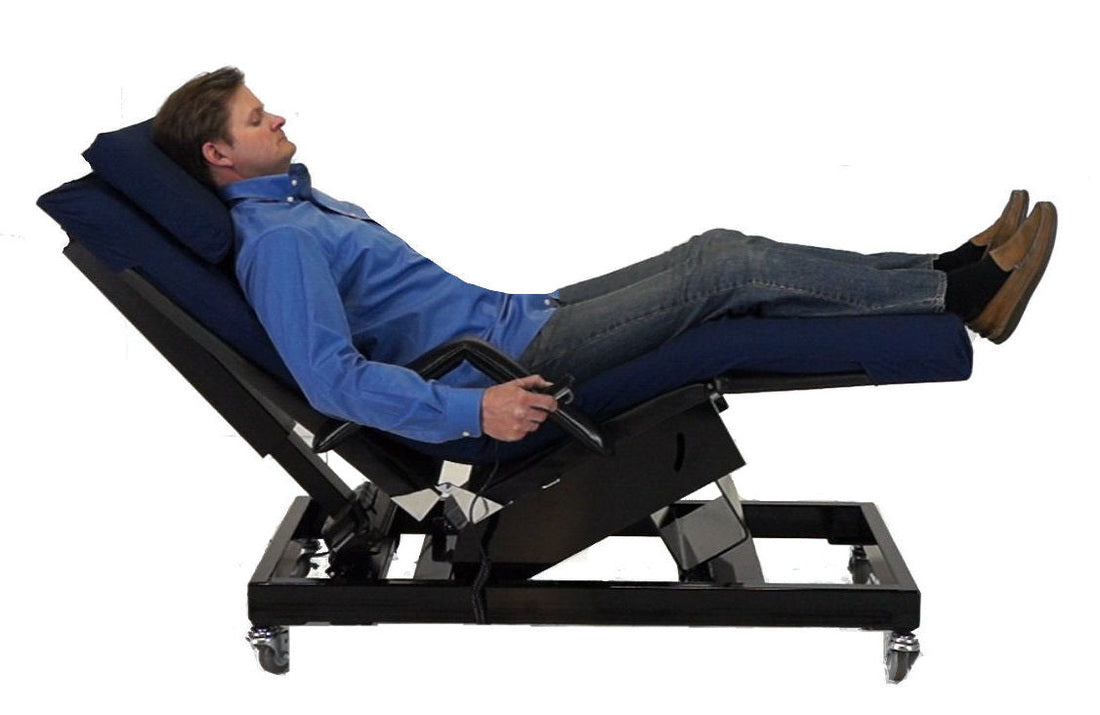 A man reclining on a black motorized adjustable bed with dark blue cushions, shown against a plain white background. Zero Gravity Chair 5 Special Needs Computers.ca