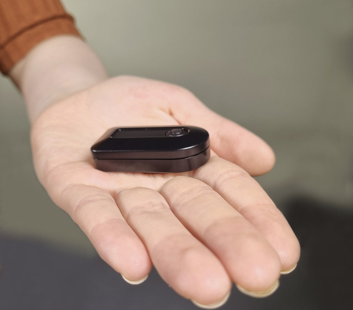 A small black rectangular electronic device with rounded corners, resting on an open palm.