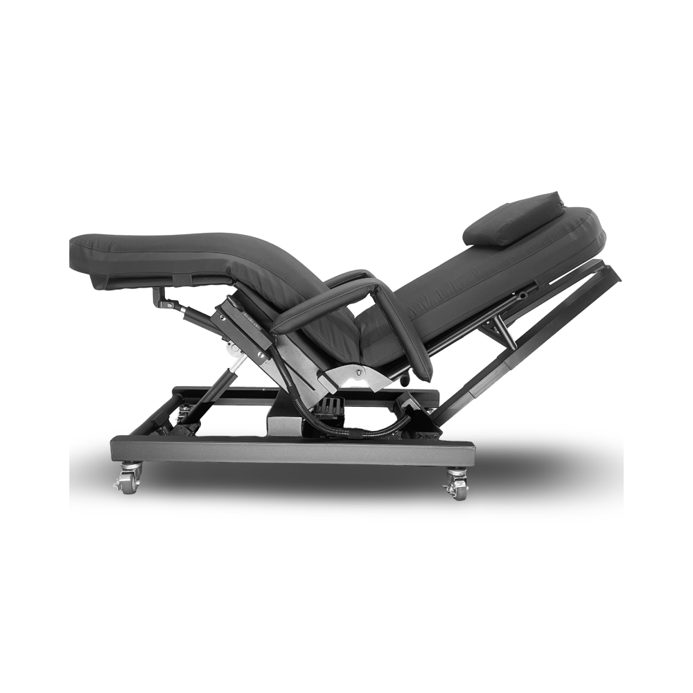 An adjustable electric massage or therapy table with padded black upholstery and a dark metal wheeled base, shown in a side profile on a white background. Zero Gravity Chair 4 Special Needs Computers.