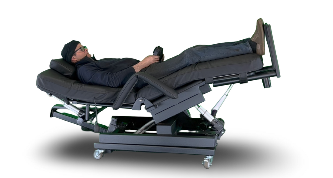 A person reclining on a motorized electric treatment bed with adjustable back and leg support, shown against a plain white background. Zero Gravity Chair 4-Lift. Special Needs Computers.ca