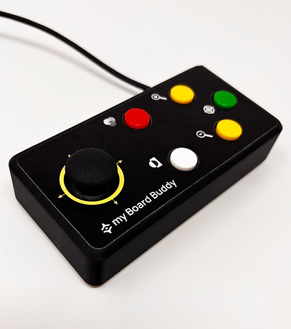 A black handheld electronic control device labeled 'my Board Buddy' with a large black joystick, yellow and green buttons, a red button, and a white button, shown on a plain light background. Special Needs Computers
