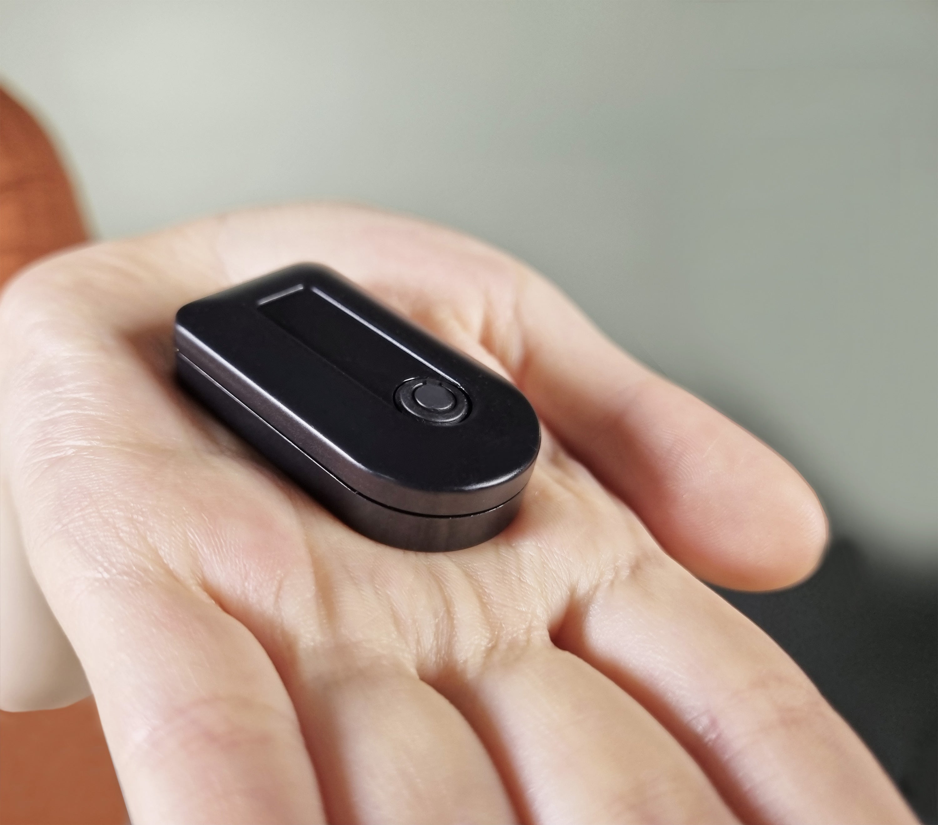 A small black oval electronic device with a power button, resting on an open hand.