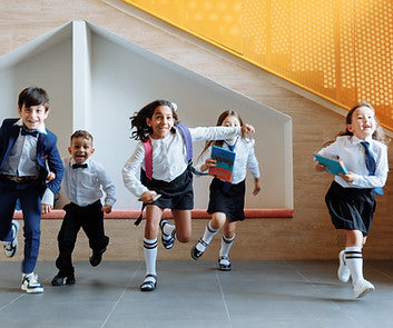 Five children in school uniforms running and jumping in a brightly lit indoor hallway with a yellow patterned wall. Special Needs Computers