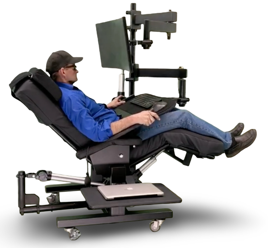 A man reclining in a black ergonomic computer chair with an attached monitor, keyboard tray, and laptop shelf on a white background.  Zero Gravity Workstation 1c. Special Needs Computers Canada.