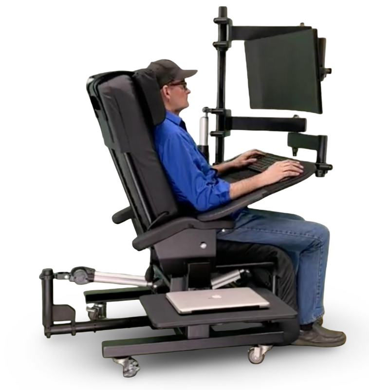 A man seated in a black ergonomic medical-style chair with a built-in keyboard tray, laptop shelf, and dual monitor arm, shown against a plain white background.  Zero Gravity Workstation 1c. Special Needs Computers Canada.