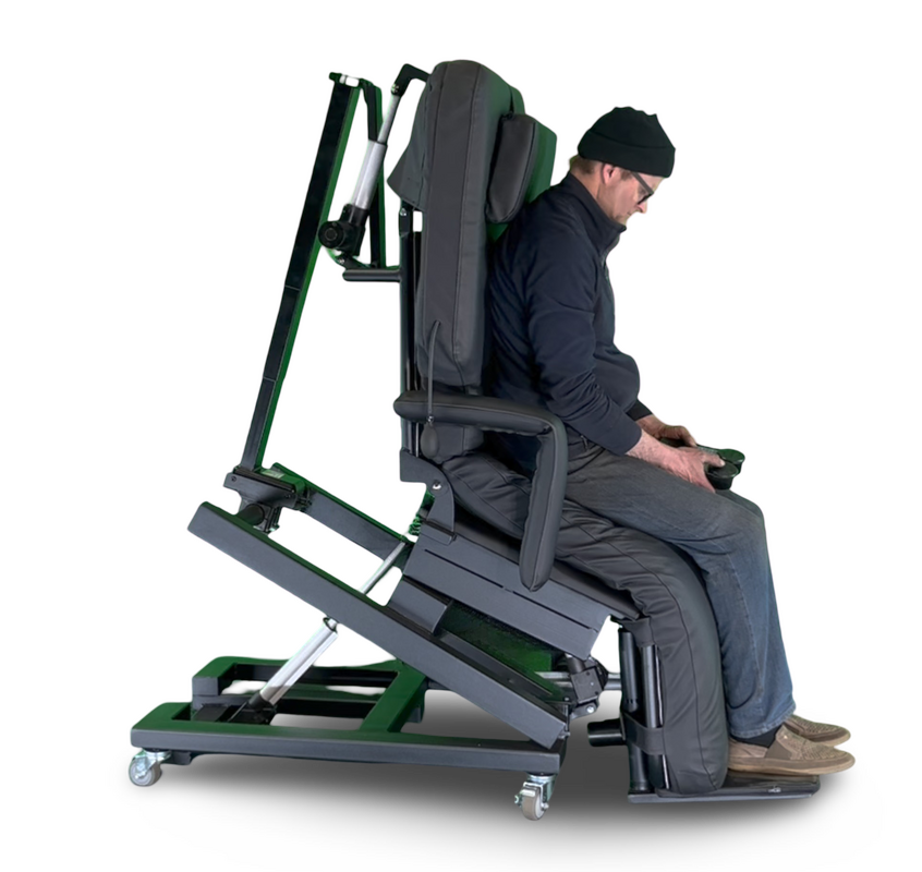 A man wearing a black beanie and dark clothing sits in a motorized standing frame device with a padded backrest and footrest, shown from the side against a plain white background.  Zero Gravity Chair 4-Lift. Special Needs Computers.ca