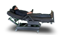 An adjustable electric hospital-style bed with a patient reclining on it, shown against a plain white background with a drop shadow.  Zero Gravity Chair 4-Lift. Special Needs Computers.ca